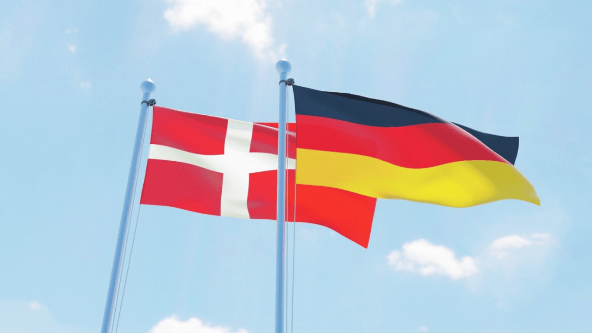 Two flags waving on flagpoles against a blue sky: the Danish flag on the left with a white cross on a red background, and the German flag on the right with horizontal black, red, and yellow stripes.