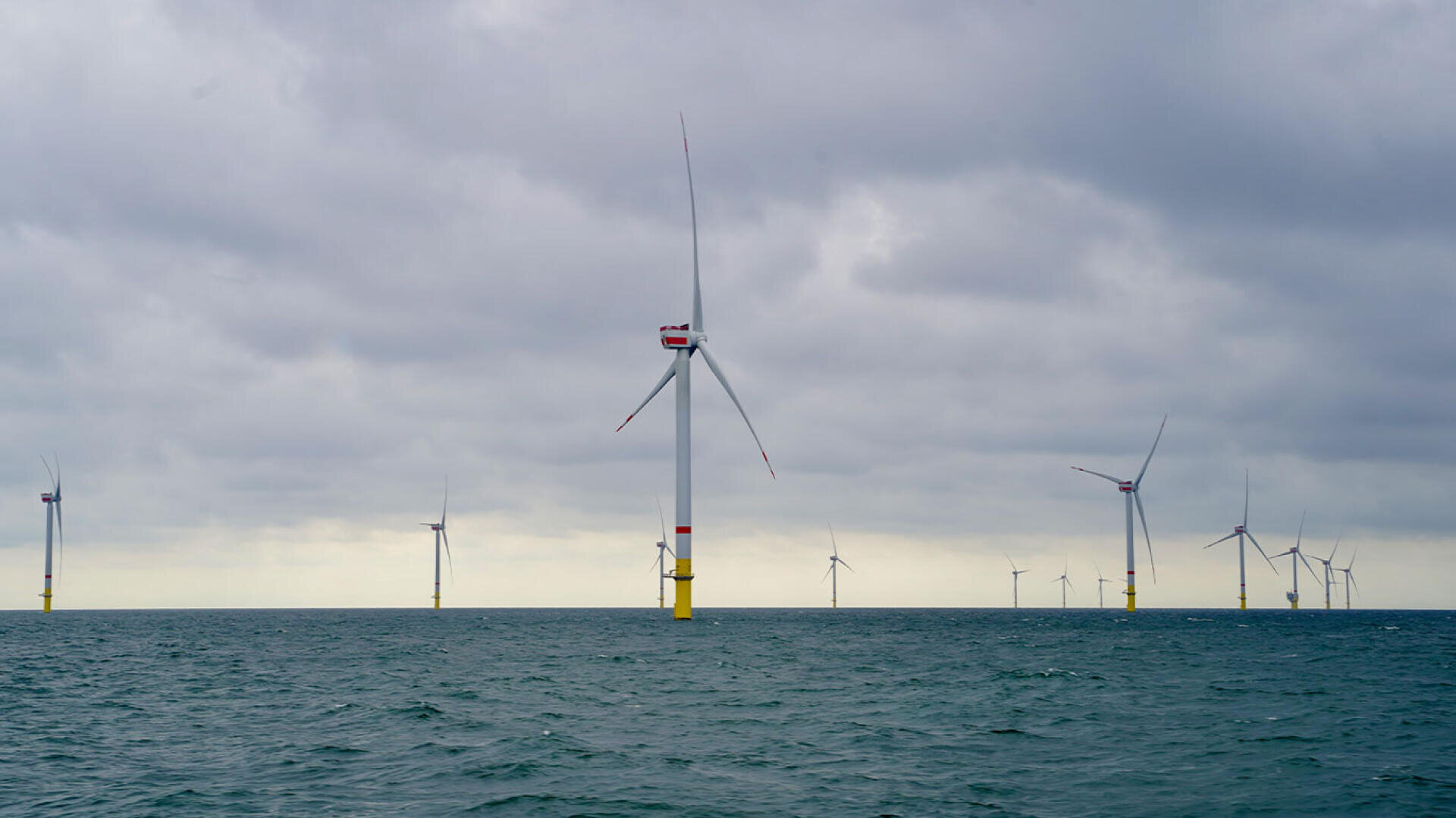 Eine Reihe von Offshore-Windkraftanlagen, die unter bewölktem Himmel im Meer stehen.