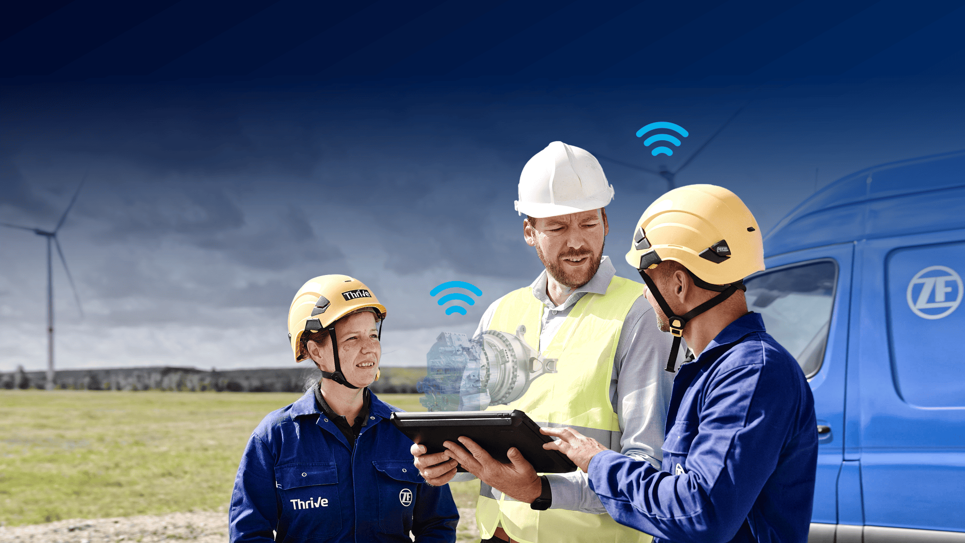 Drei Arbeiter in Schutzkleidung stehen im Freien neben einem blauen Lieferwagen mit einer Windkraftanlage im Hintergrund. Einer hält ein Tablet in der Hand, auf dem ein digitales Motormodell mit drahtlosen Symbolen zu sehen ist, was auf eine technologiegestützte Zusammenarbeit hindeutet.