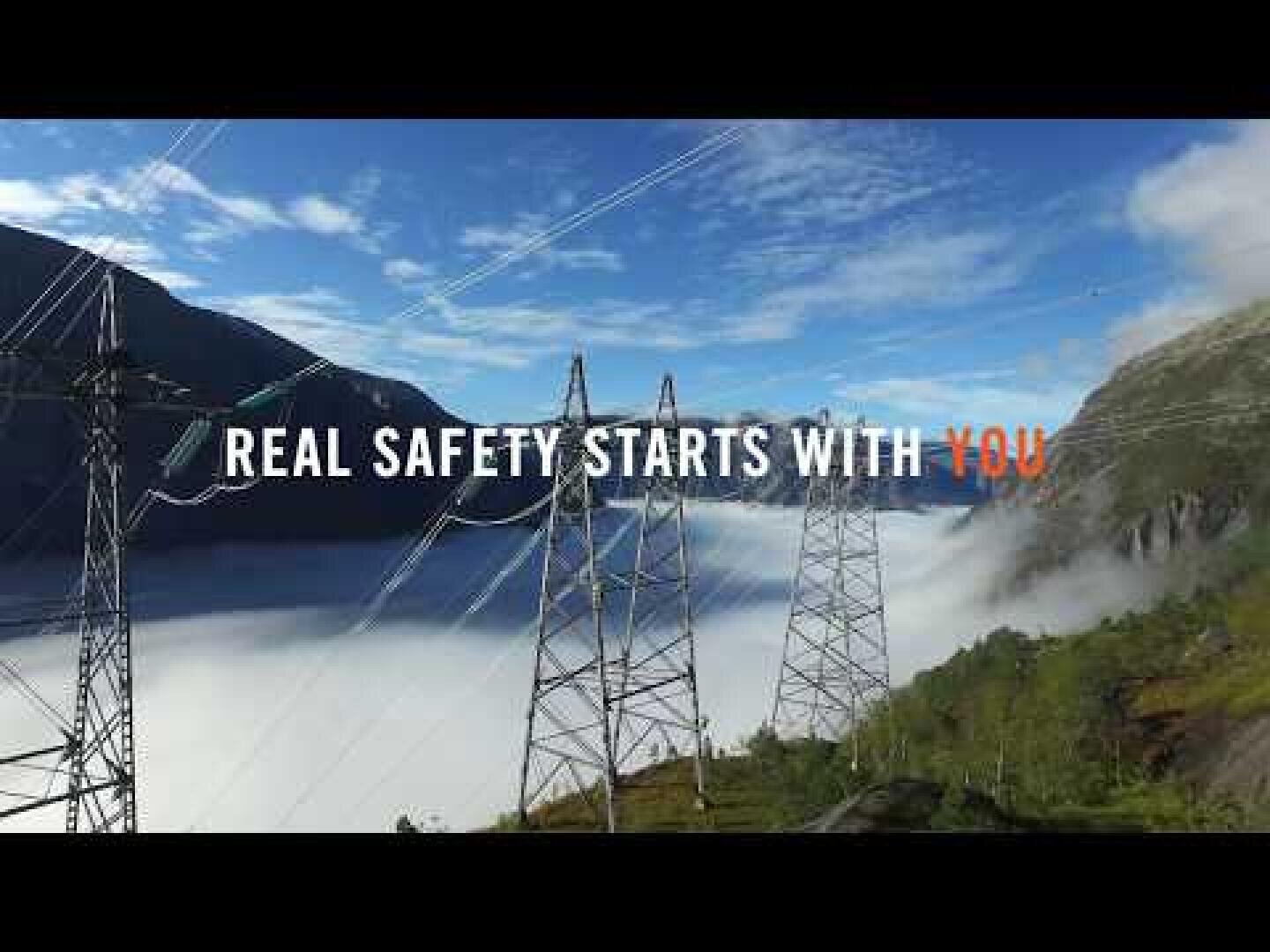Hochspannungsleitungen erstrecken sich unter blauem Himmel durch ein nebliges Bergtal. Der Text „ECHTE SICHERHEIT BEGINNT BEI DIR“ ist über das Bild gelegt, wobei DU orange hervorgehoben ist.